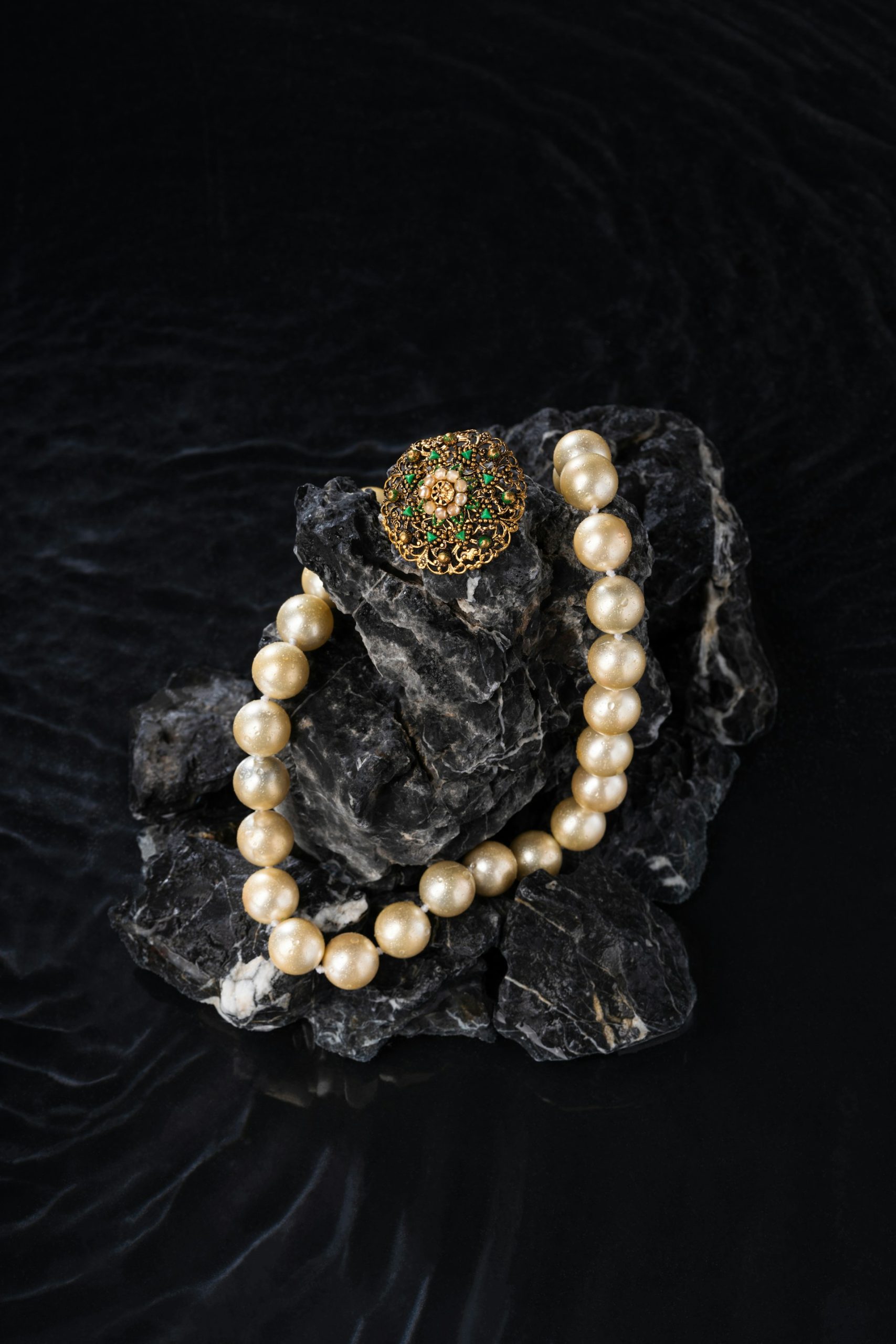 Pearl necklace and brooch on dark rocks